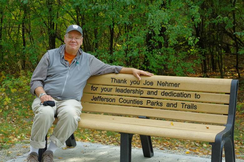 Parks Director Joe Nehmer sitting on recognition bench with incription