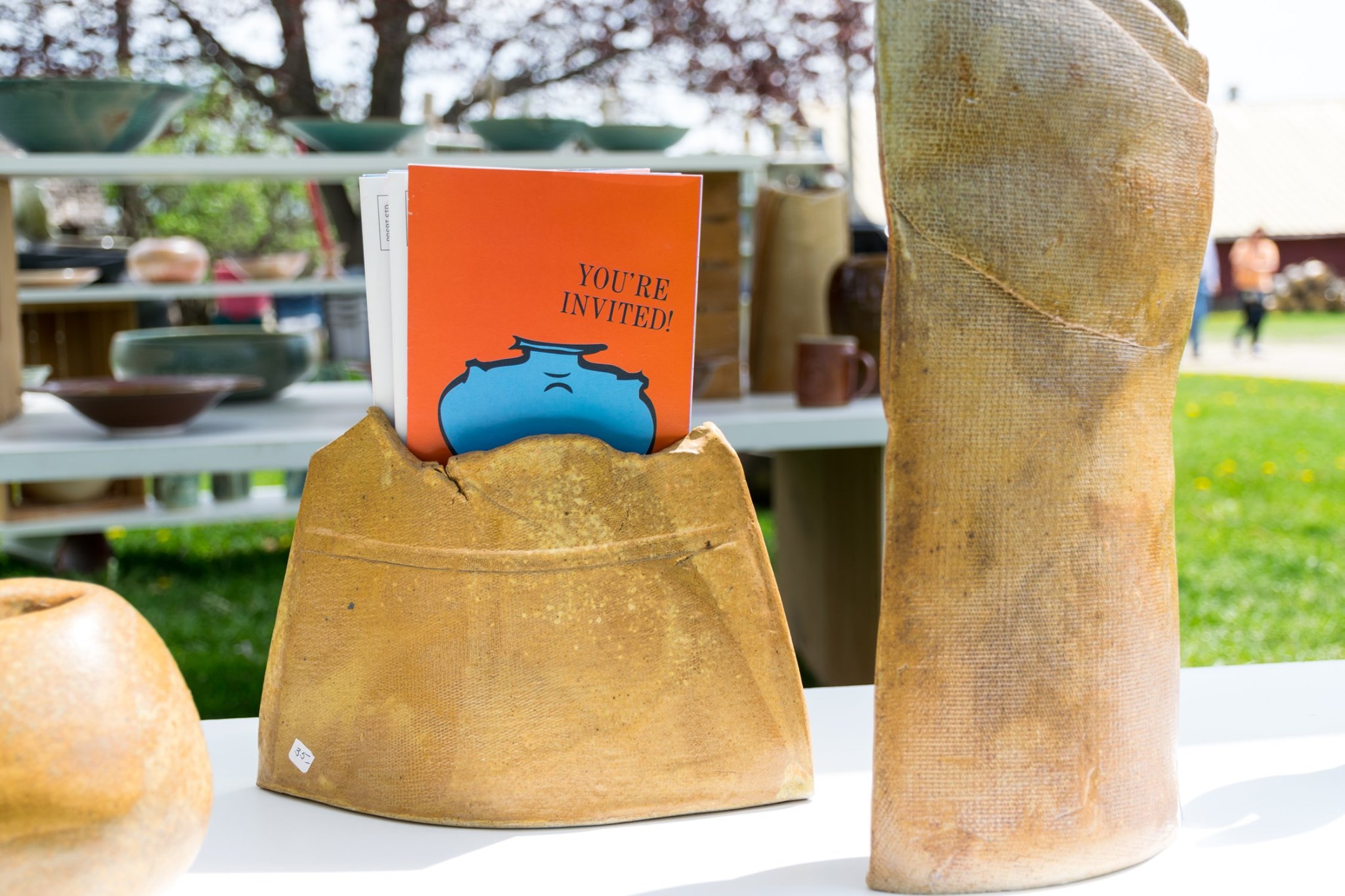 Clay Collective brochure sticking out of pottery on table outdoors