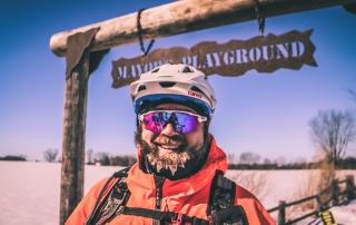 Biker with frozen beard and orange jacket with sunglasses smiling